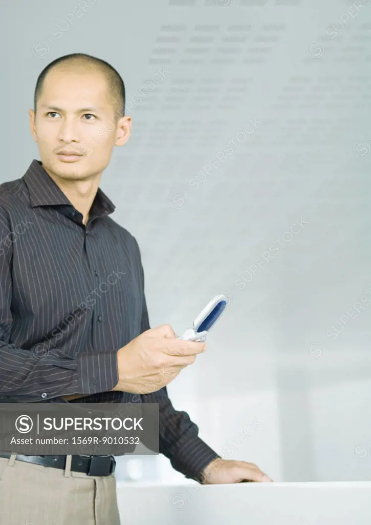 Businessman standing with cell phone in hand, looking to the side