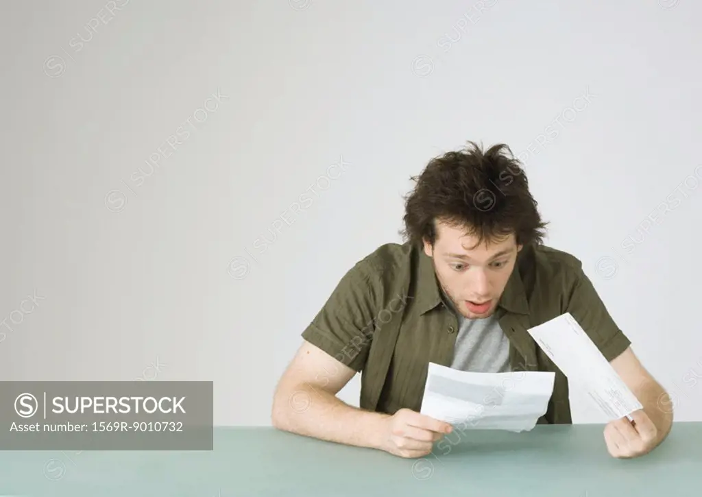Young man looking at letter, reacting with surprise