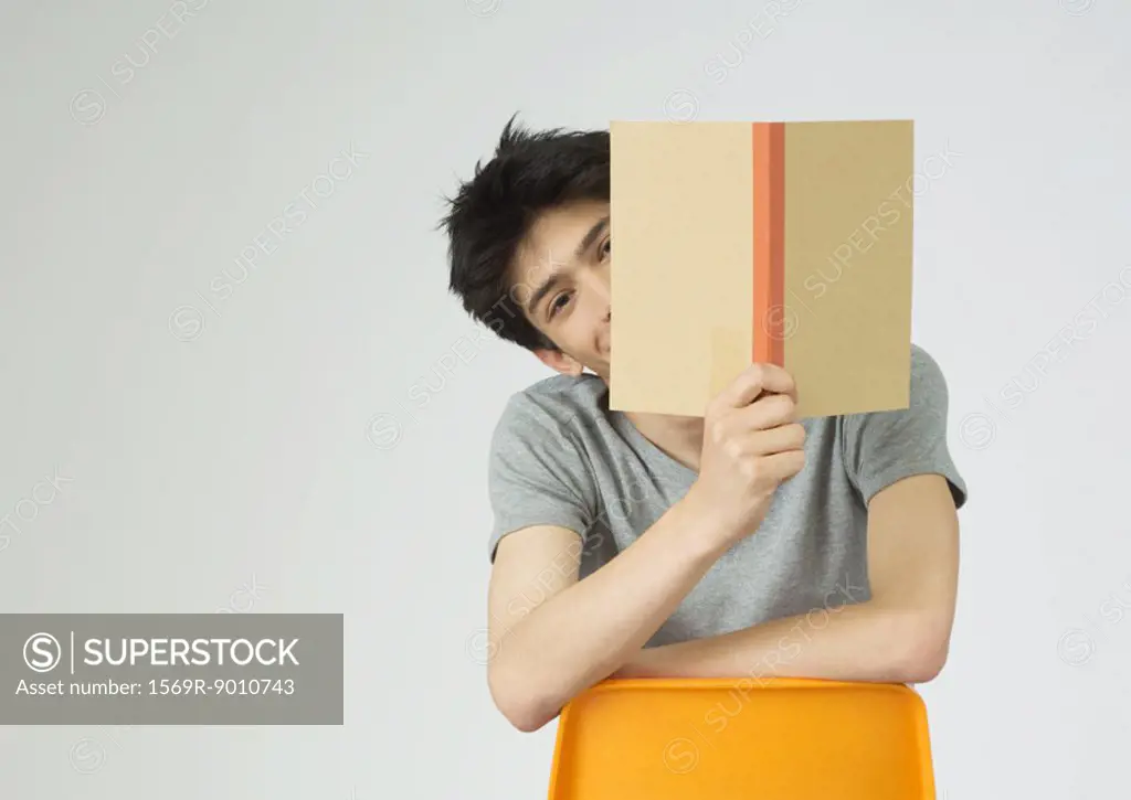 Young man holding up book, peeking around the edge of it
