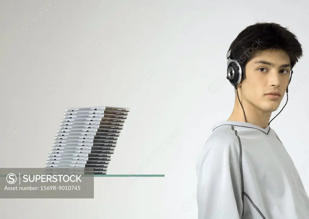 Young man listening to headphones, next to stack of cds
