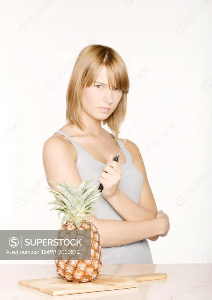 Woman holding up knife next to pineapple