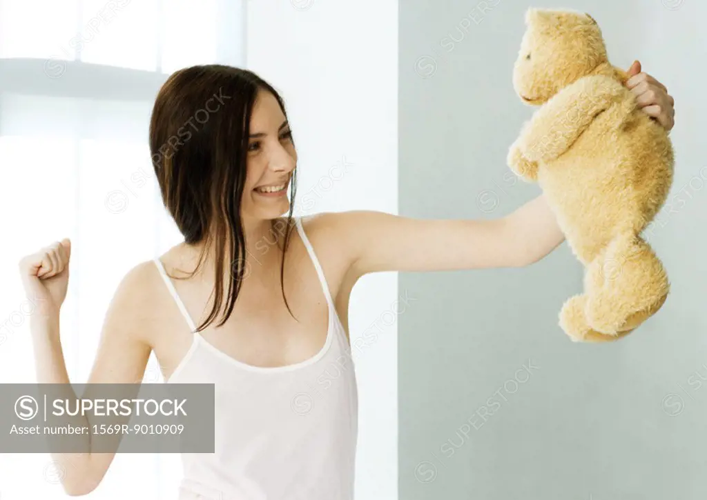 Young woman holding up teddy bear and making fist