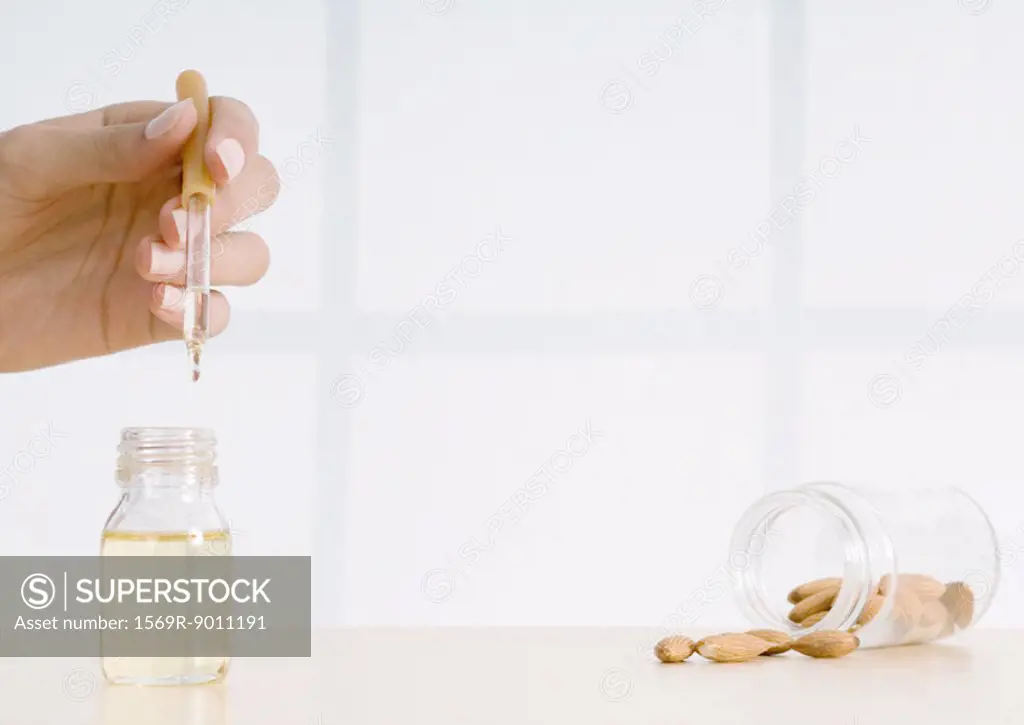 Woman´s hand holding essential oil dropper and almonds spilling from jar