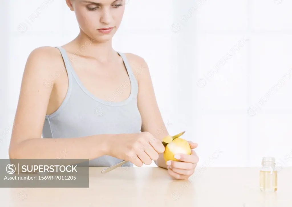 Woman peeling lemon near bottle of essential oil
