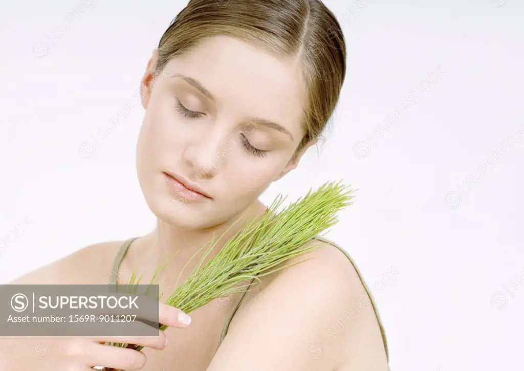 Woman holding sprig of pine, eyes closed