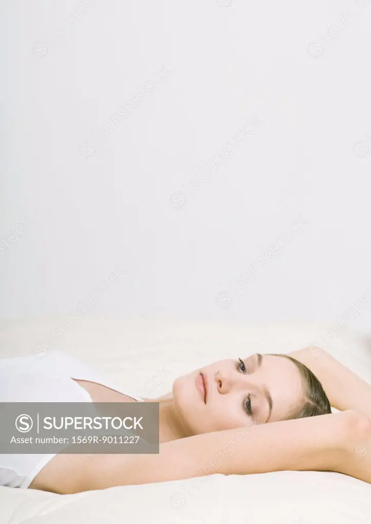 Woman lying back on bed with arms over head