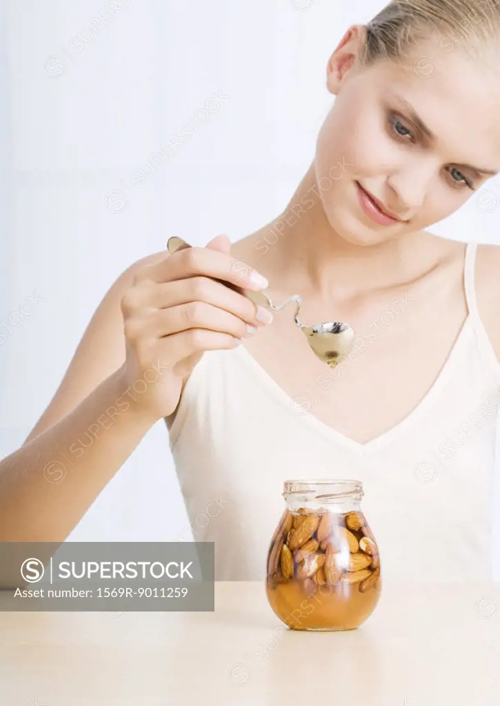 Woman holding spoon over jar of almonds and honey