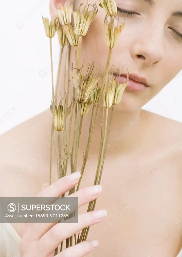 Woman with eyes closed holding dried flowers against face