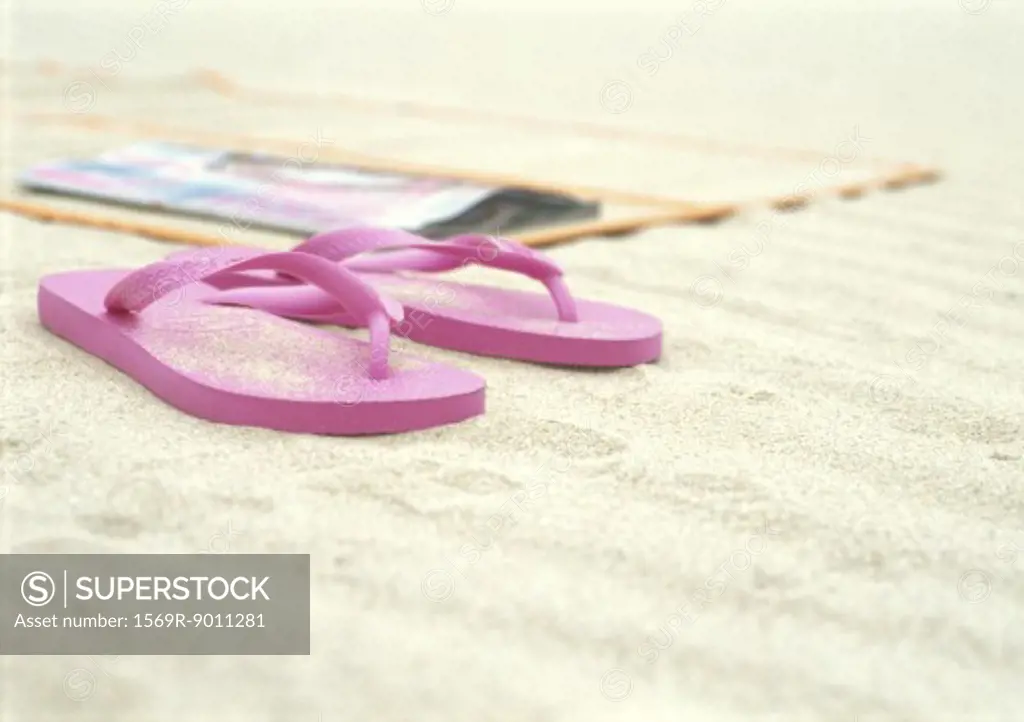 Pink flipflops next to beach mat on beach