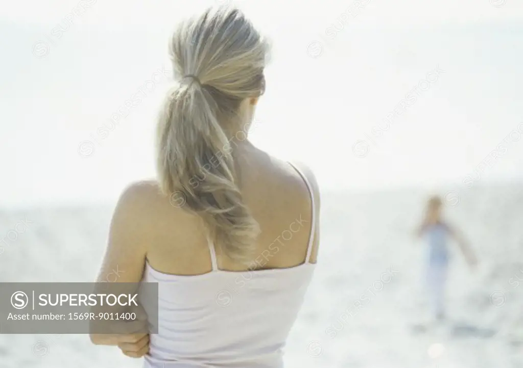 Woman looking toward child on beach, rear view