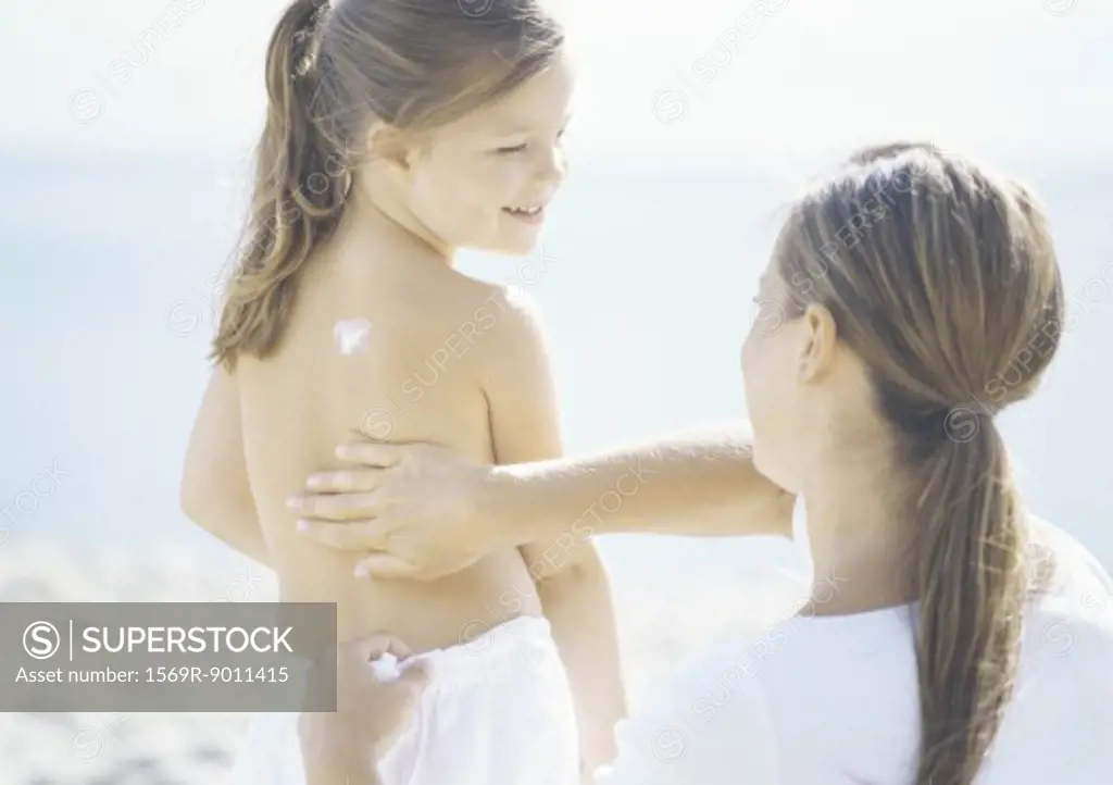 Woman rubbing sunscreen into girl's back