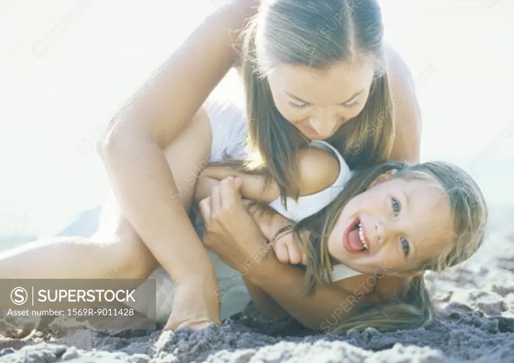 Woman holding daughter on sand, laughing