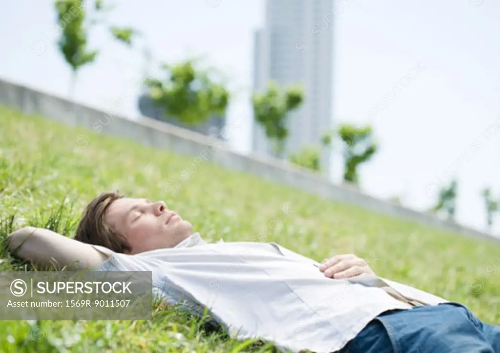 Young man lying on grass in urban park