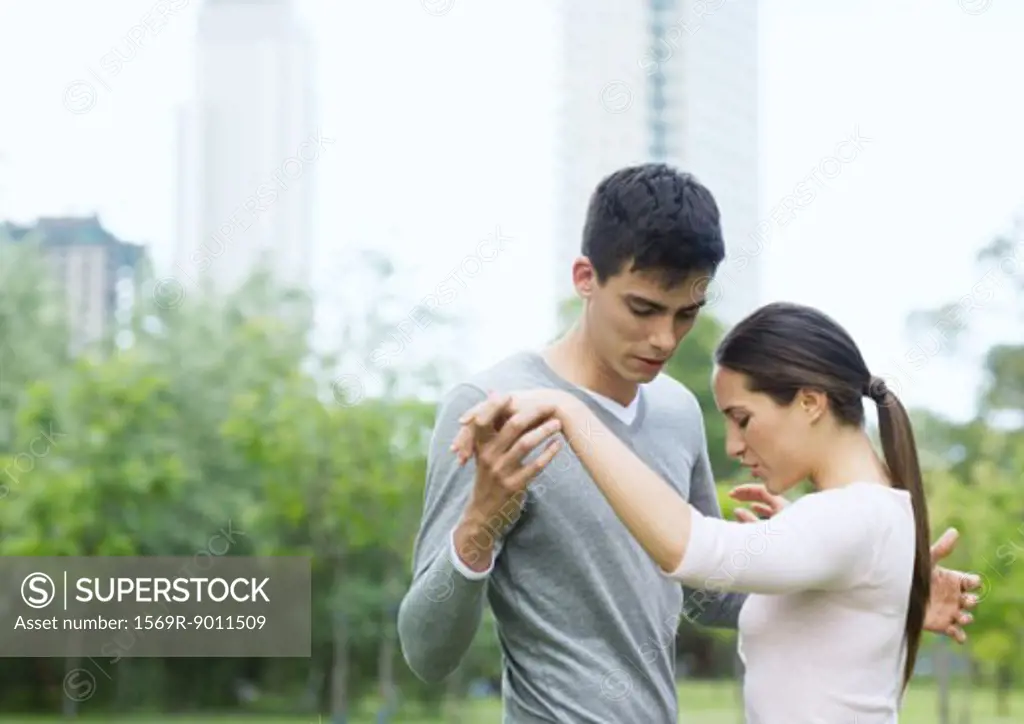 Young woman teaching young man to dance in urban park