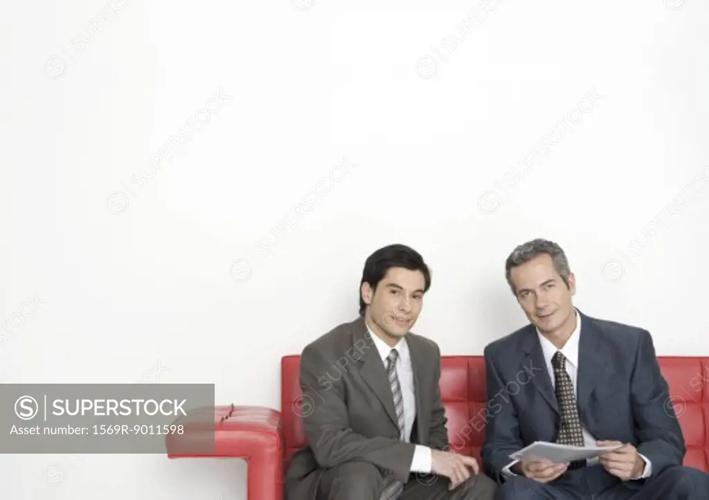 Two businessmen sitting on couch, one holding document