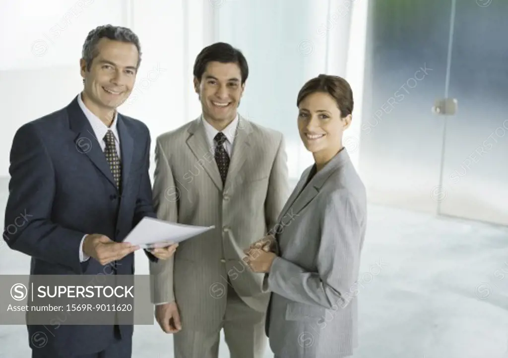 Three business associates standing in lobby, smiling