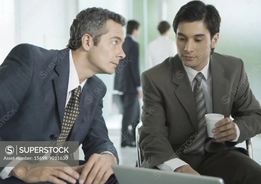 Two businessmen sitting around laptop, one with coffee cup