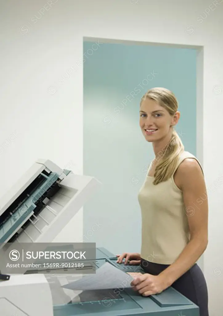 Female office worker standing at copy machine, smiling at camera