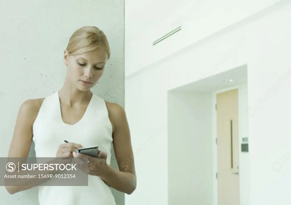 Woman using electronic organizer in hallway of office building