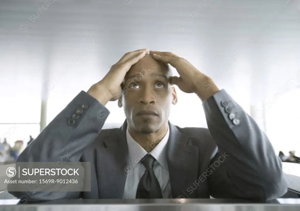 Businessman looking up and holding head in airport