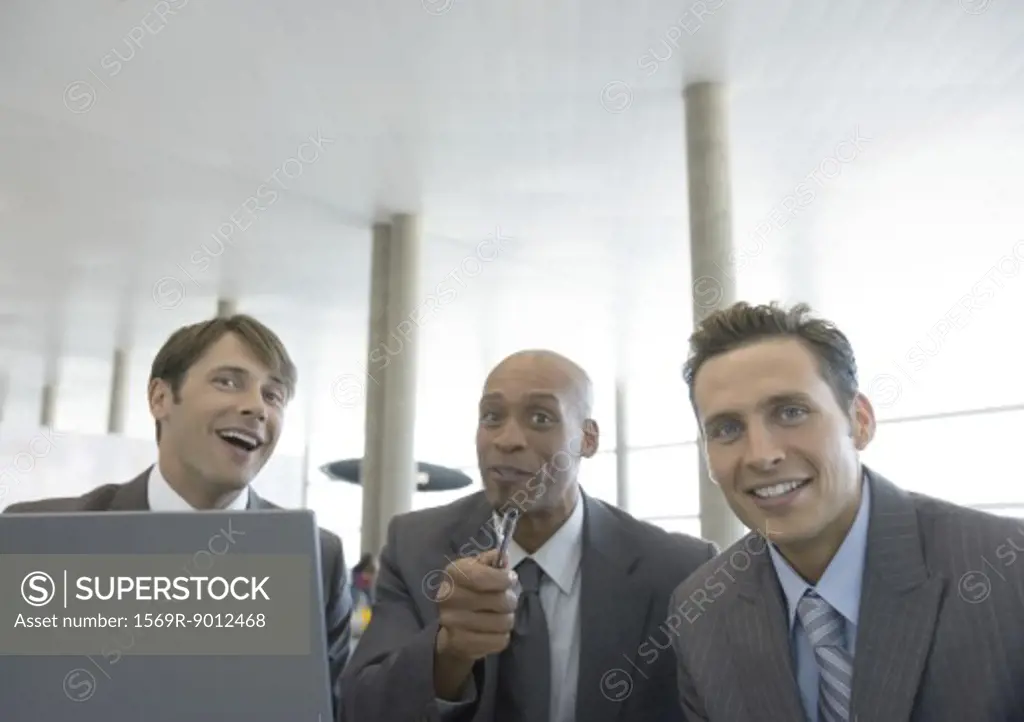 Three businessmen with laptop, smiling and pointing at camera