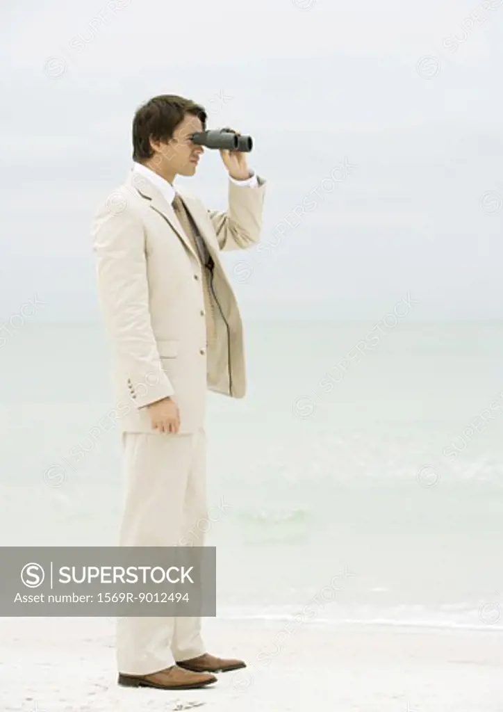 Businessman using binoculars on beach