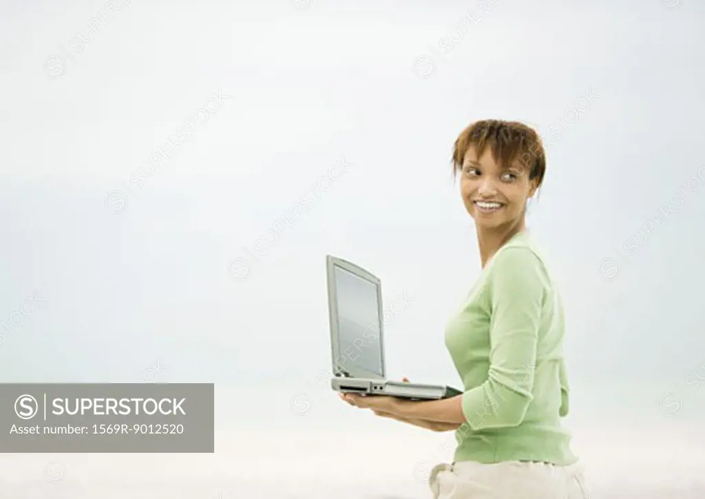 Woman holding open laptop, looking over shoulder