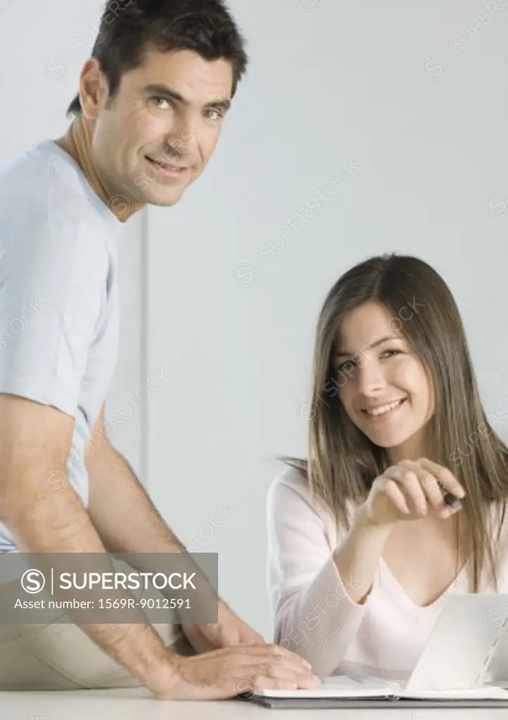 Couple working on budget together, smiling at camera