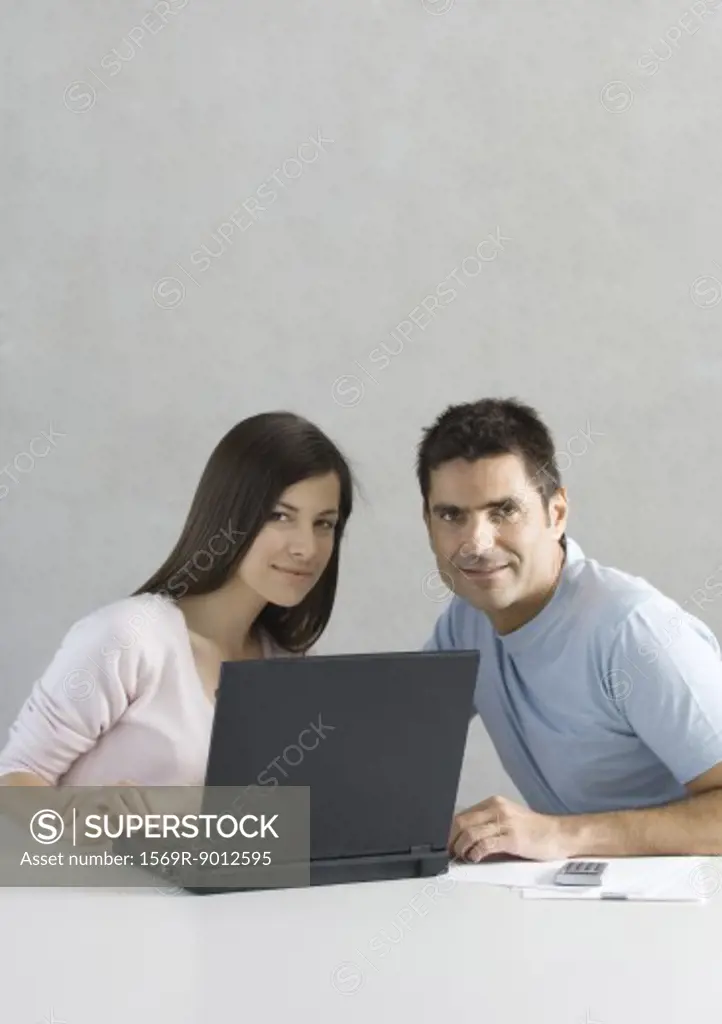 Couple using laptop, smiling at camera