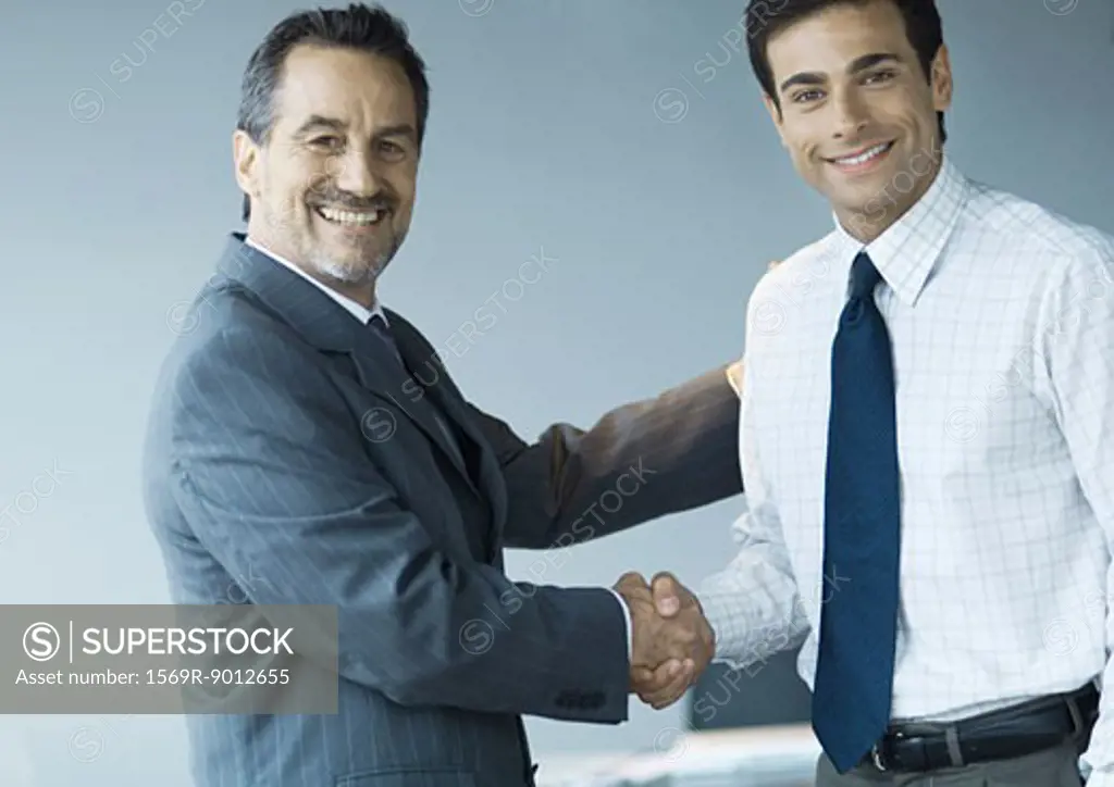 Business executives shaking hands, smiling at camera