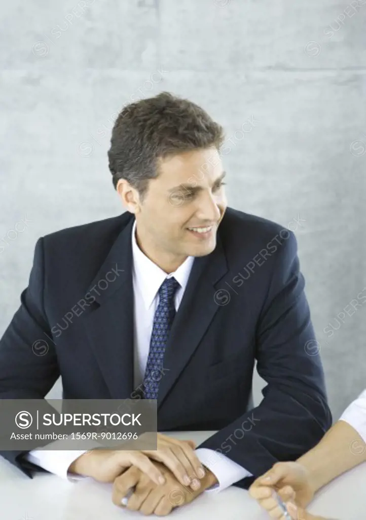 Businessman sitting at table, smiling at colleague