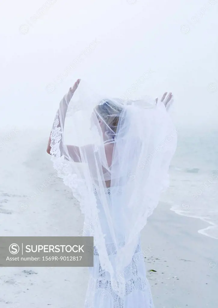 Bride holding up veil on beach