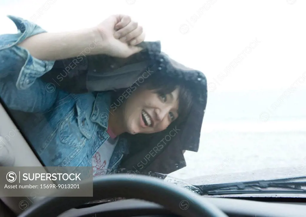 Woman looking through windshield, holding jacket over head