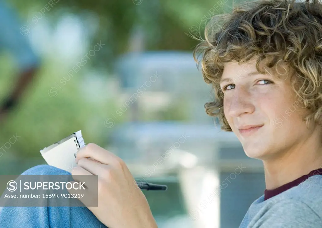 Teenage boy sitting with pen and notebook, side view