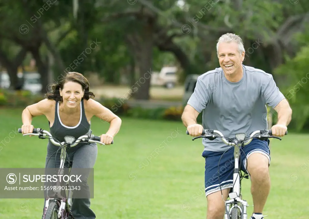 Mature couple riding bikes, front view