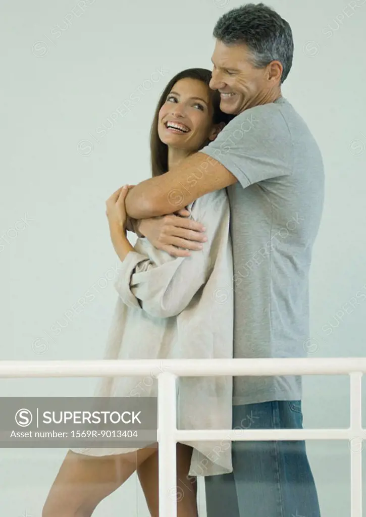 Couple smiling at each other, man standing behind woman with arms around her