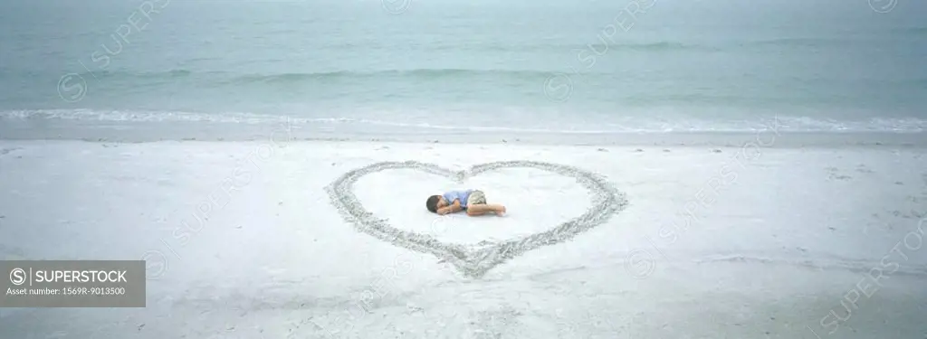 Child lying inside heart drawn on beach