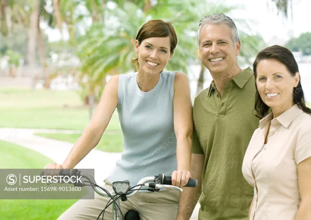 Three adult friends smiling at camera, one on bike