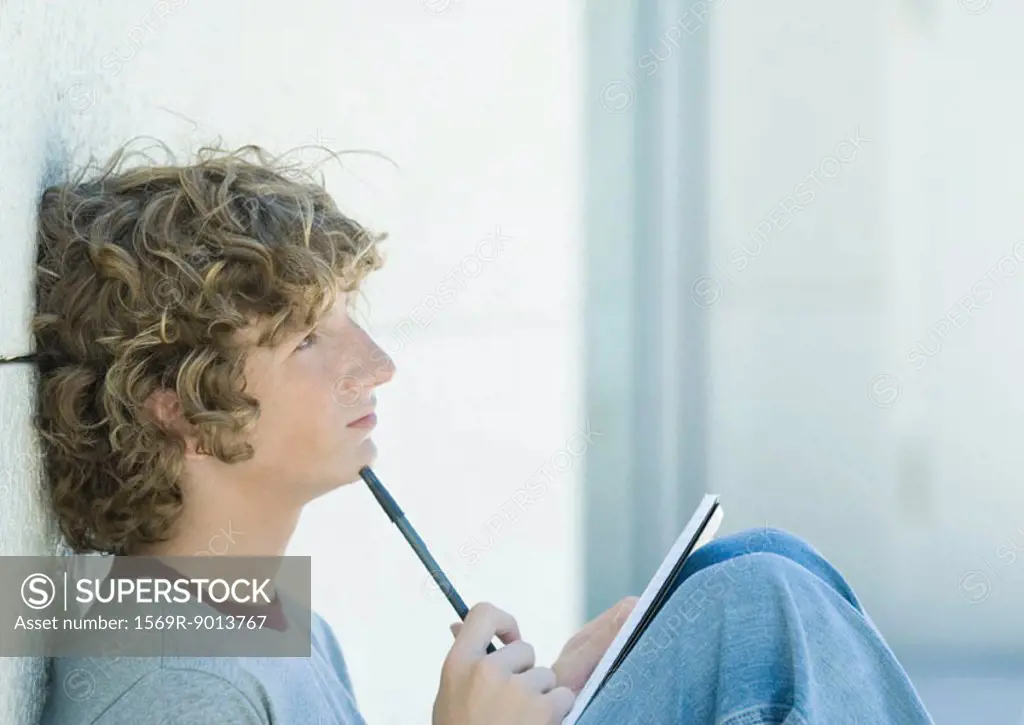 Teenage boy sitting with pen and notebook, side view