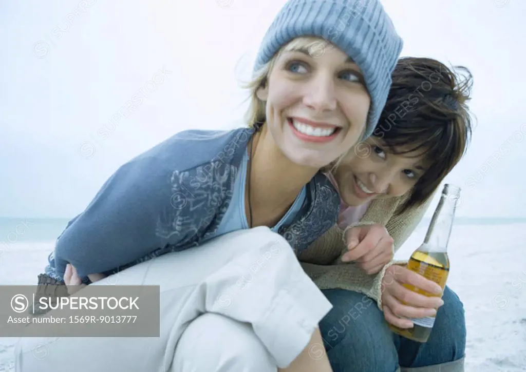 Two female friends on beach, one with bottle of beer