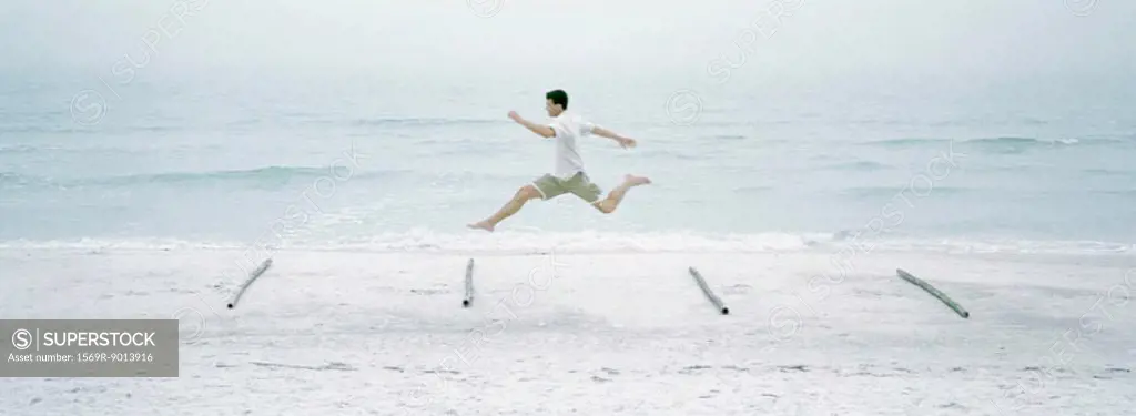 Man running and jumping over logs on beach