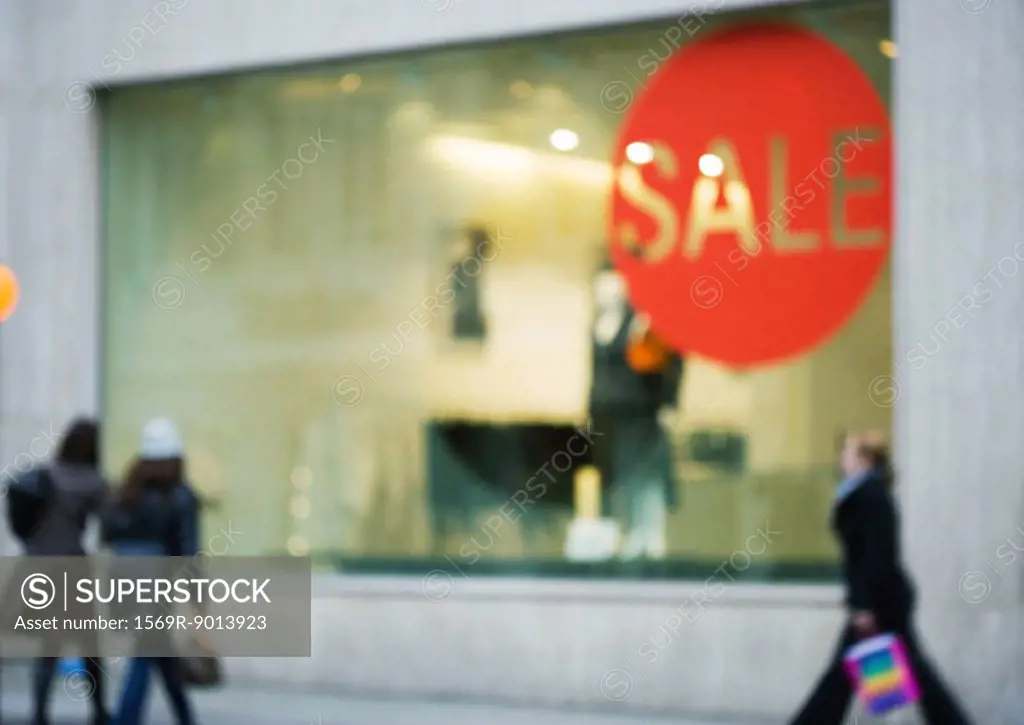 Shop window with sale sign, shoppers walking by