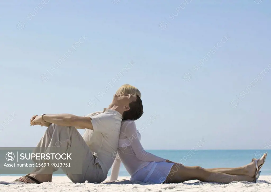 Couple sitting back to back on beach