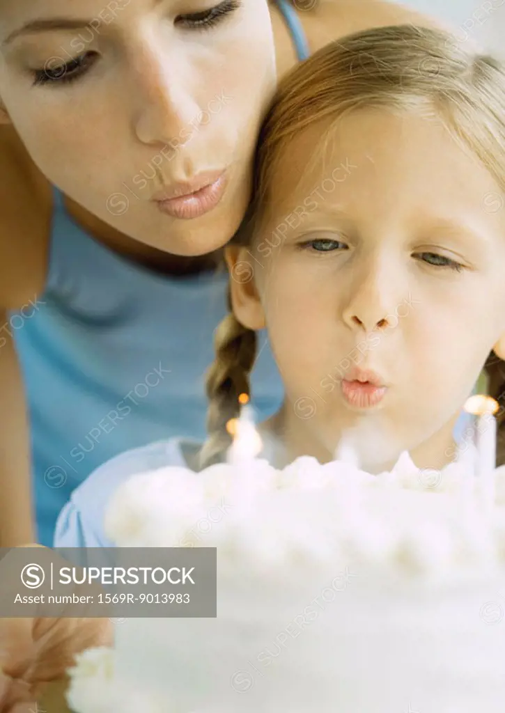 Mother and girl blowing out candles on birthday cake
