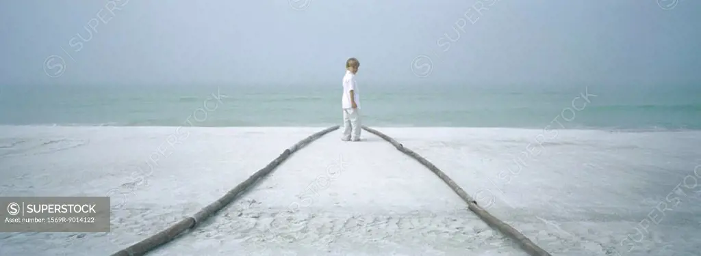 Boy standing at end of path on beach, looking over shoulder