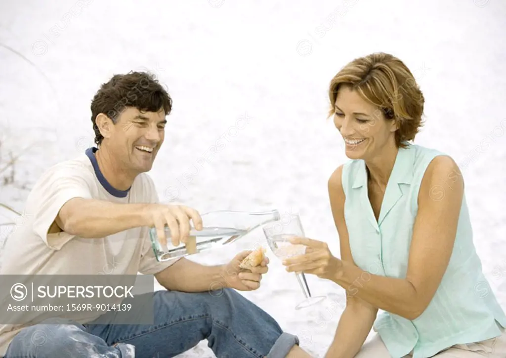Man pouring woman glass of water on beach