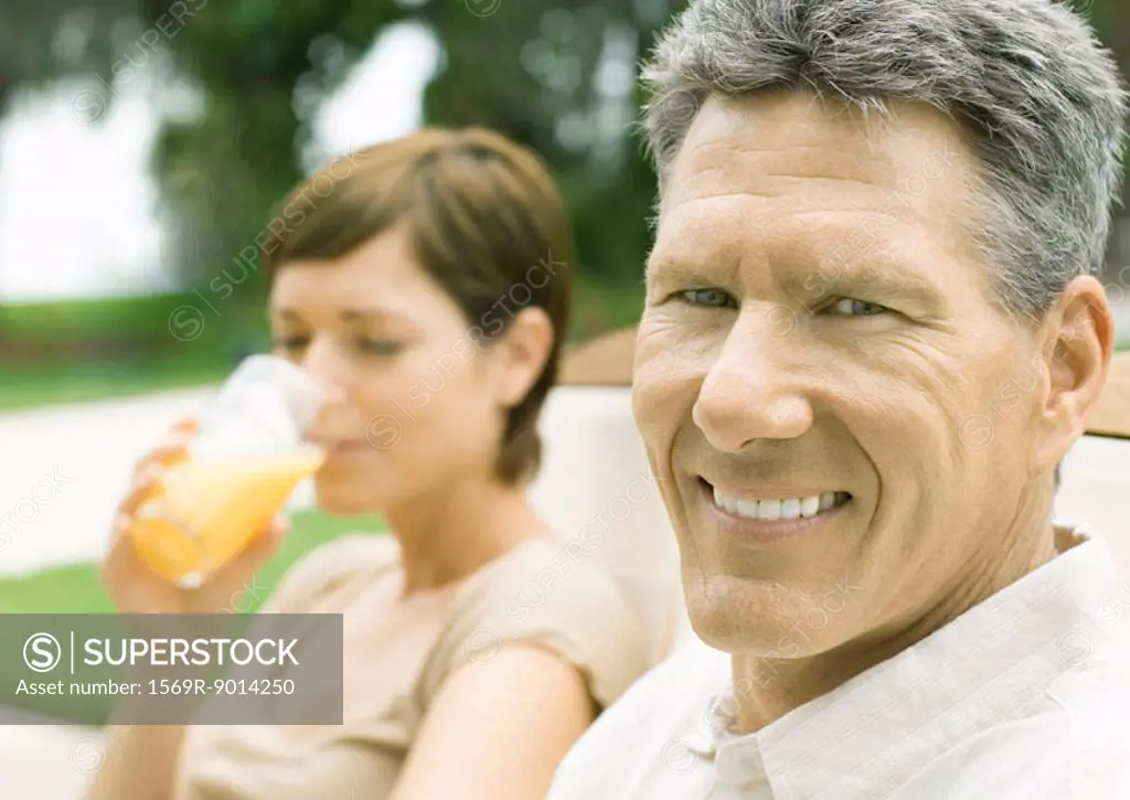 Man smiling as woman drinks juice in background