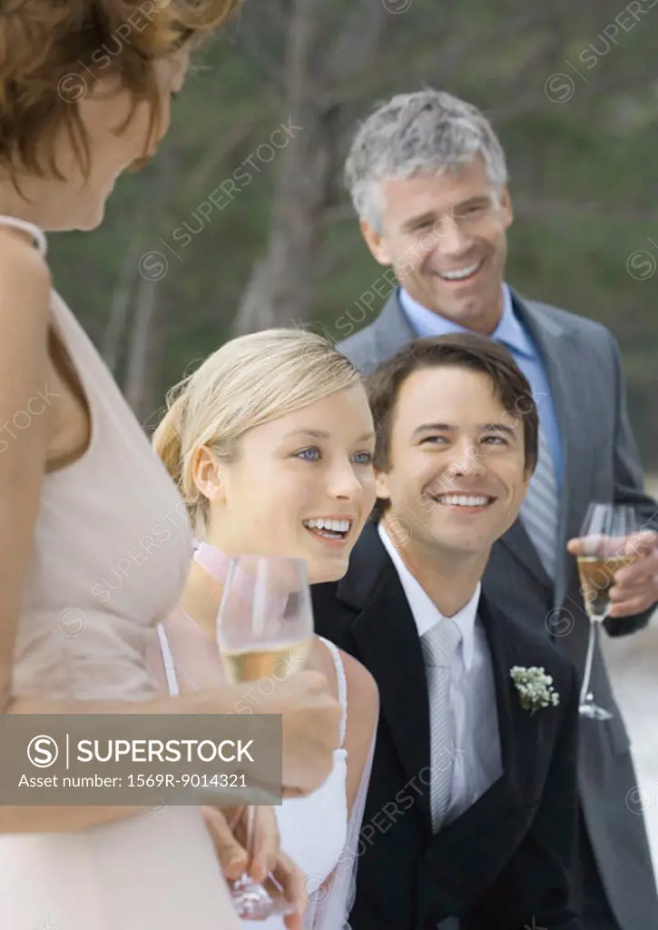 Outdoor wedding party, young bride and grooming standing between mature man and woman