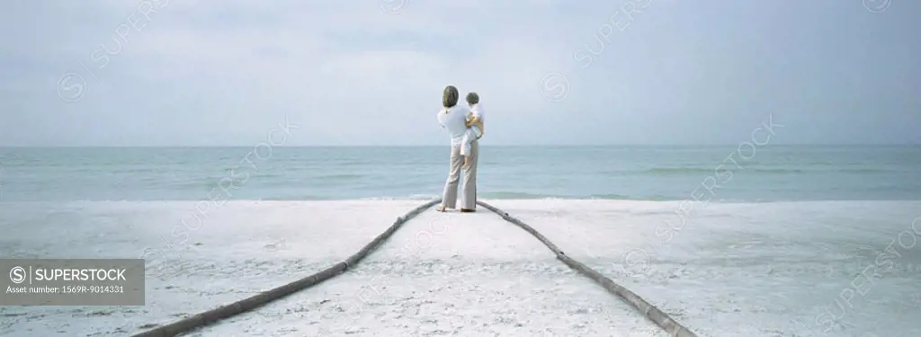 Mother and child standing at end of path on beach