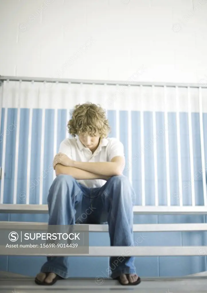 Teen boy sitting with head down on gym bleachers